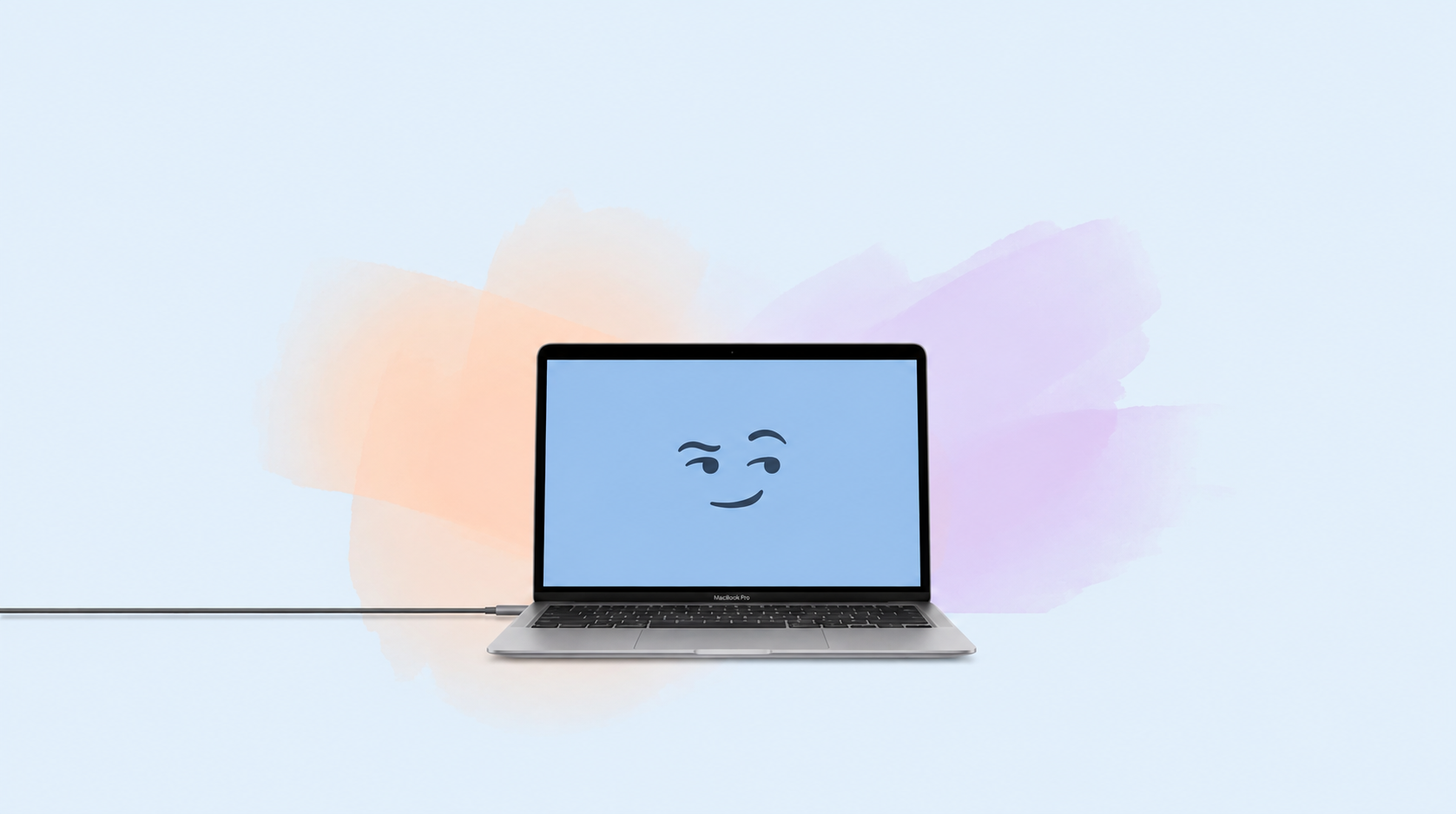 A silver MacBook with a mischievous face on its blue screen, connected to its charger.